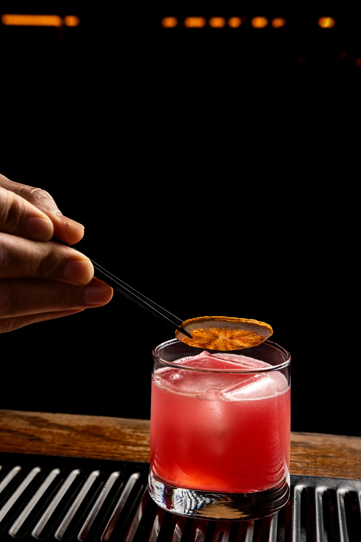 A bartender garnishes a red Oak and Iron cocktail with dried citrus